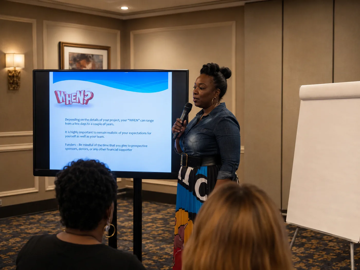 Workshop facilitator speaking to attendees beside a presentation screen